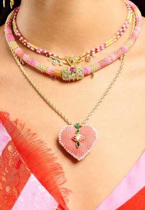 Des colliers superposés colorés présentent des perles multicolores, des éléments métalliques dorés, et un pendentif en forme de cœur orné d'un travail de perles complexe et de décorations.