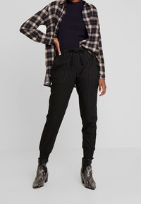 Czarno-białe spodnie w paski z elastycznym pasem, zestawione z kraciastą, oversize'ową koszulą oraz metalicznymi botkami na obcasie w wzór węża.