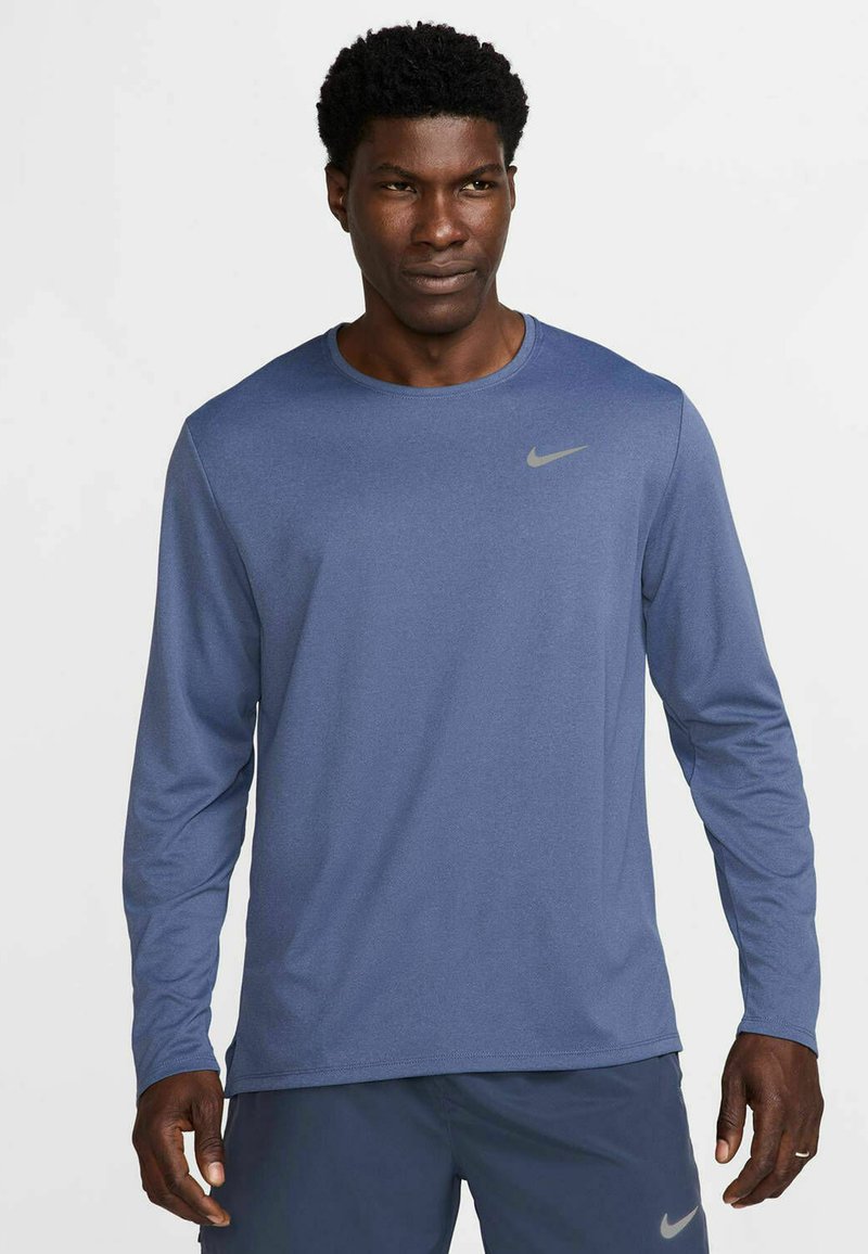 Langærmet atletisk skjorte i marineblåt stof med en glat tekstur. Har et lille gråt Nike-logo på den øverste venstre bryst.