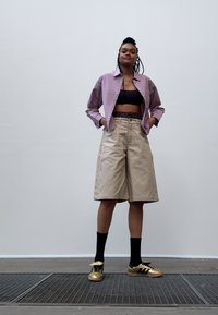 Ljuslila rutigt skjorta, svart crop top, beige knälånga shorts, svarta strumpor och guld-svarta sneakers. Inga ytterligare mönster eller detaljer.