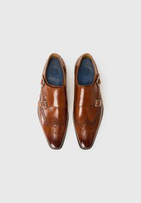 Brune lærdress sko med spiss tå, dekorativ brogue-detaljering, og sølvfargede spenne på hver side. Glatt tekstur.