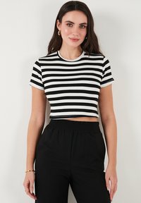 Mustriga must-valge lühikeste varrukatega crop top, ümmarguse kaelusega, pehme ja veniva kangaga ning keha lähedase lõikega.