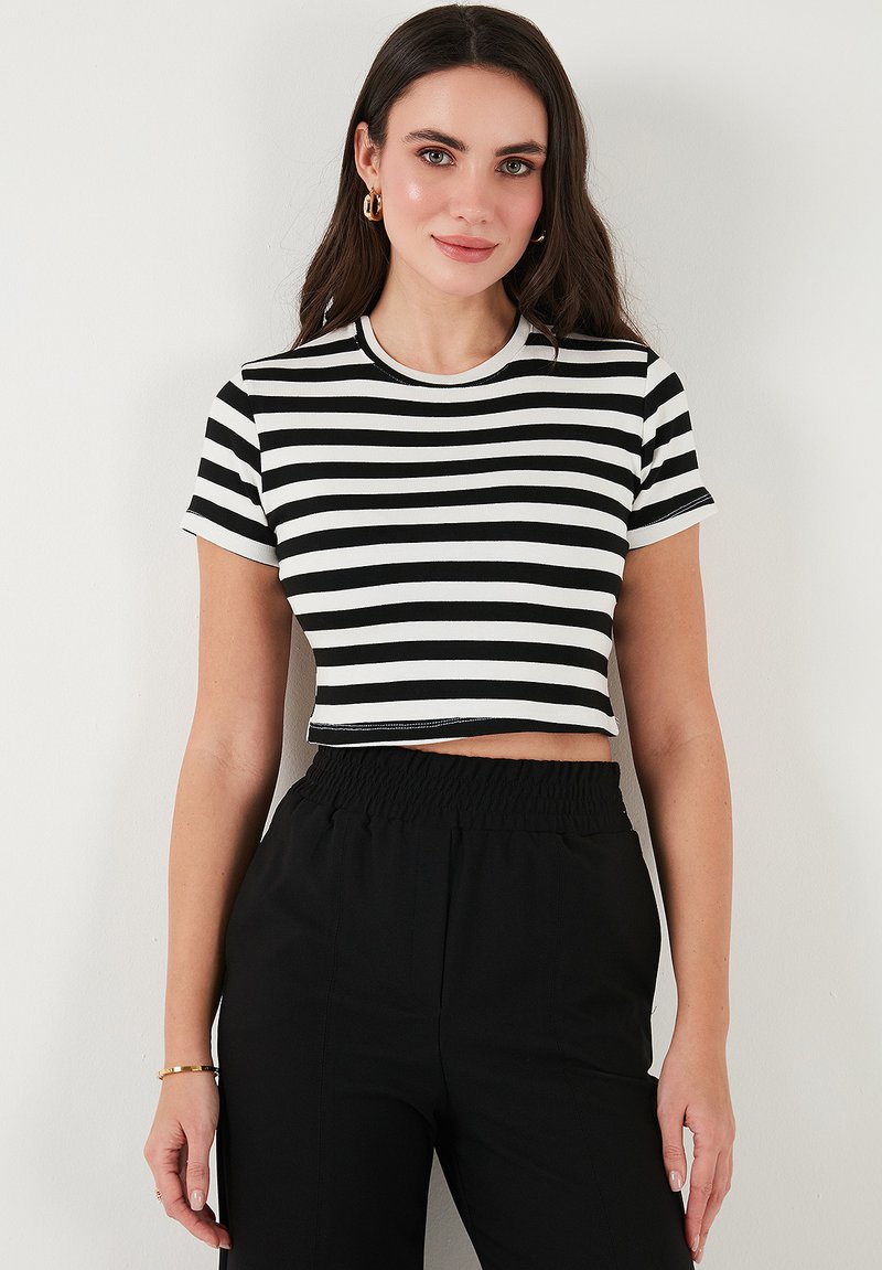 Mustriga must-valge lühikeste varrukatega crop top, ümmarguse kaelusega, pehme ja veniva kangaga ning keha lähedase lõikega.