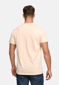 Koszulka krótko rękawowa w jasnym odcieniu brzoskwiniowym, z okrągłym dekoltem, uszyta z miękkiego materiału, o gładkiej teksturze i prostym, schludnym designie.