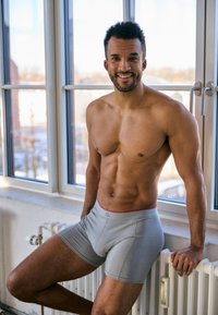 Boxer briefs grigio chiaro con un elastico rosso, texture liscia, design aderente e lunghezza a metà coscia, esposte su un modello maschile.