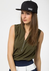 Black snapback cap with "VANS" logo, olive green sleeveless top with a front zip, paired with a textured navy and white skirt.