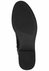 Suela de zapato negra con patrón de agarre texturizado, forma redondeada y ligero tacón. Presenta bordes suaves y un sutil detalle de marca.