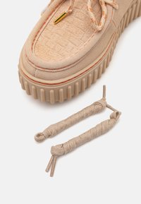 Baskets en daim beige avec un dessus texturé, des coutures orange et une semelle en caoutchouc épaisse. Comprend deux lacets beiges torsadés.