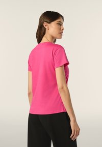 Camiseta ajustada de manga corta en algodón rosa vibrante, con un cuello redondo y una textura suave, mostrada desde la parte de atrás.