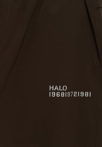 Bruine stof met een gladde textuur met op de voorkant de witte bedrukte tekst "HALO 196819721981". Eenvoudig ontwerp zonder extra accenten.