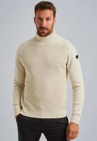 Beige Strickrollkragenpullover mit gerippten Bündchen und Saum. Besitzt ein strukturiertes Muster auf der Vorderseite und schlichte Ärmel. Hergestellt aus weichem Stoff.