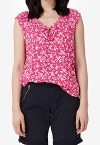 Top sin mangas con estampado floral en rosa, con escote en V y detalle de lazo. Tejido suave, corte relajado, combinado con pantalones cortos de un azul marino oscuro.