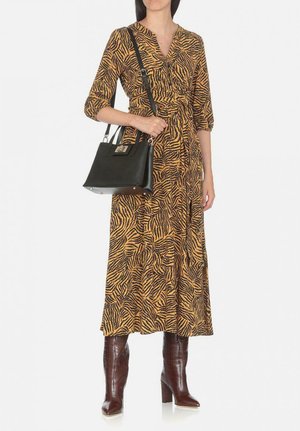 Long yellow dress with black tiger stripes, cinched waist, three-quarter sleeves; paired with a black handbag and brown heeled boots.