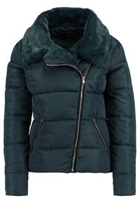 Teal vadderad jacka med fuskpälskrage och dragkedja framtill. Har ett horisontellt quiltat mönster och sidfickor med dragkedja. Mjuk textur.