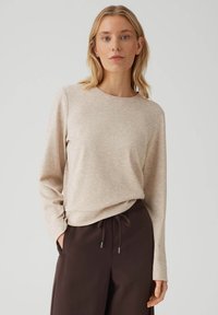 Beige top met lange mouwen gemaakt van zacht materiaal met een ronde hals, gecombineerd met donkerbruine broek met elastische tailleband en trekkoord.