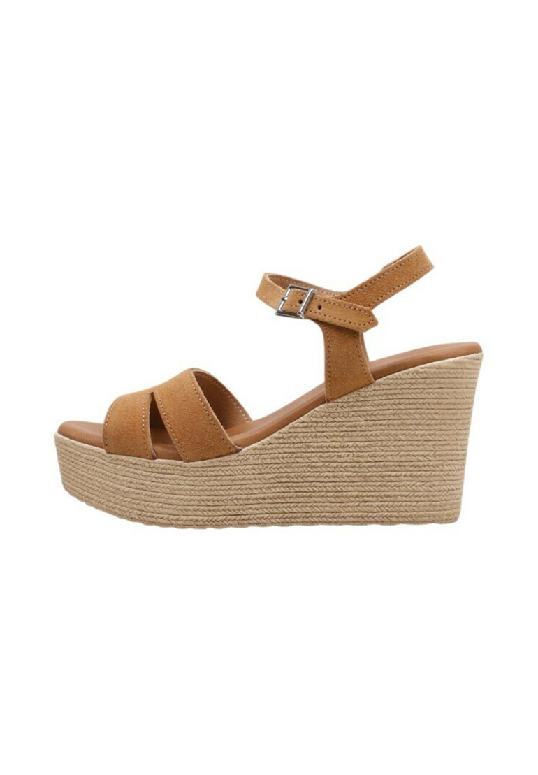 Sandalias de cuña de ante en color beige con una plataforma de yute trenzado, que presentan dos correas cruzadas y una correa ajustable en el tobillo con un hebilla de metal.