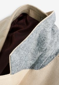 Bolsa de tela beige con un cuello de fieltro gris, con un forro interior marrón texturizado, acabada con costuras limpias y una forma estructurada.