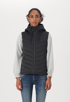 Gilet rembourré noir avec capuche, présentant un design matelassé en chevrons, des poches zippées et des manches longues grises portées en dessous.