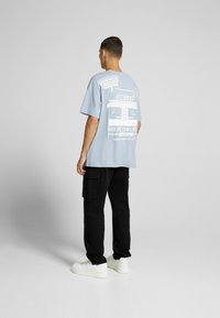 Ljusblå grafisk t-shirt med text och illustrationer av en hamburgerrestaurang på baksidan, kombinerad med svarta cargobyxor och vita sneakers.