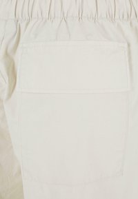 Beige stoffshorts med en samlet elastisk midje og en enkelt baklomme med flat klaff. Glatt tekstur og minimalt design.