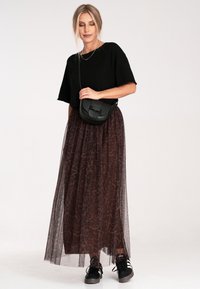 Czarna bluzka z krótkim rękawem, brązowa spódnica maxi z tulle w leoparda i czarna torebka na ramię. W zestawie z czarnymi sneakersami, prezentując warstwowy wygląd.