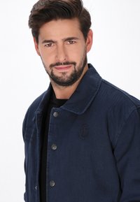 Tengerészkék farmerdzseki gallérral, gombos záródással és hímzett horgonylogóval a mellkason. Sima tapintású és laza dizájnú.