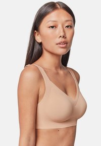 Sujetador inalámbrico en color nude, con una tela suave y elástica, correas ajustables y un diseño en V. Apariencia minimalista y sin costuras.