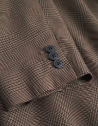 Tecido texturizado castanho com um padrão pied-de-poule, apresentando três botões pretos numa manga, e linhas subtis em vermelho e bege entrelaçadas.