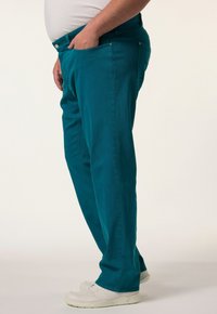 Pantalones de algodón turquesa con un diseño de pierna recta y bolsillos laterales, combinados con zapatillas blancas, vistos de lado.