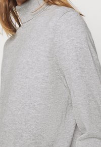 Maglione grigio a collo alto in un morbido materiale lavorato a maglia. Presenta un design aderente, un colletto a coste e una texture sottile.
