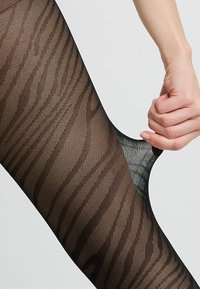 Collant neri con un design traslucido che presenta una texture a strisce zebrate. Il tessuto è elasticizzato e ha una finitura liscia.
