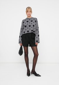 Grå, kortermet genser med svart stjernepattern, kombinert med teksturerte svarte shorts. Tilbehør inkluderer en svart veske og spisse hæler.