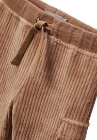 Pantalon en velours côtelé marron avec une texture ribée, doté d'une taille élastique à cordon et d'une poche latérale. Le tissu semble doux et moelleux.