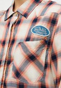 Rutet skjorte i hvitt, oransje og marineblått med brystlomme og blå Von Dutch California-logo på øvre venstre side.
