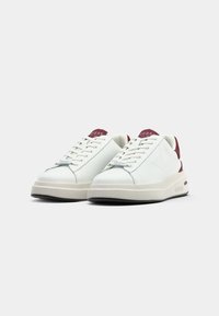 Hvite sneakers laget av glatt syntetisk materiale med burgunderfarge på hælen og tungen, med en tykk kremfarget såle og flate lisser.