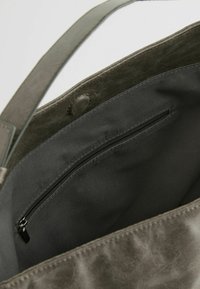 Wnętrze zielonej skórzanej torby na ramię z czarną kieszenią na zamek błyskawiczny, gładką teksturą i miękką podszewką. Posiada pojedynczy uchwyt.