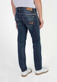 Donkerblauwe spijkerbroek met een rechte pasvorm, voorzien van twee achterzakken, een leren label bij de taille en een ritszakdetail.