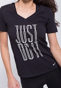 Camiseta negra de manga corta con cuello en V hecha de algodón, con el texto vertical blanco "JUST DO IT" en una fuente Negrita. Logo de Nike en la parte inferior izquierda.