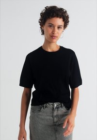 Svart t-shirt med kort ärm tillverkad av mjuk bomull. Kombinerad med en figursydd grå denimkjol. Enkel design med en klassisk rund halsringning.