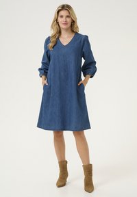 Denim jurk met een V-hals, pofmouwen en zijzakken. Tot de knie, met een rechte pasvorm en stiksels langs de onderrand.