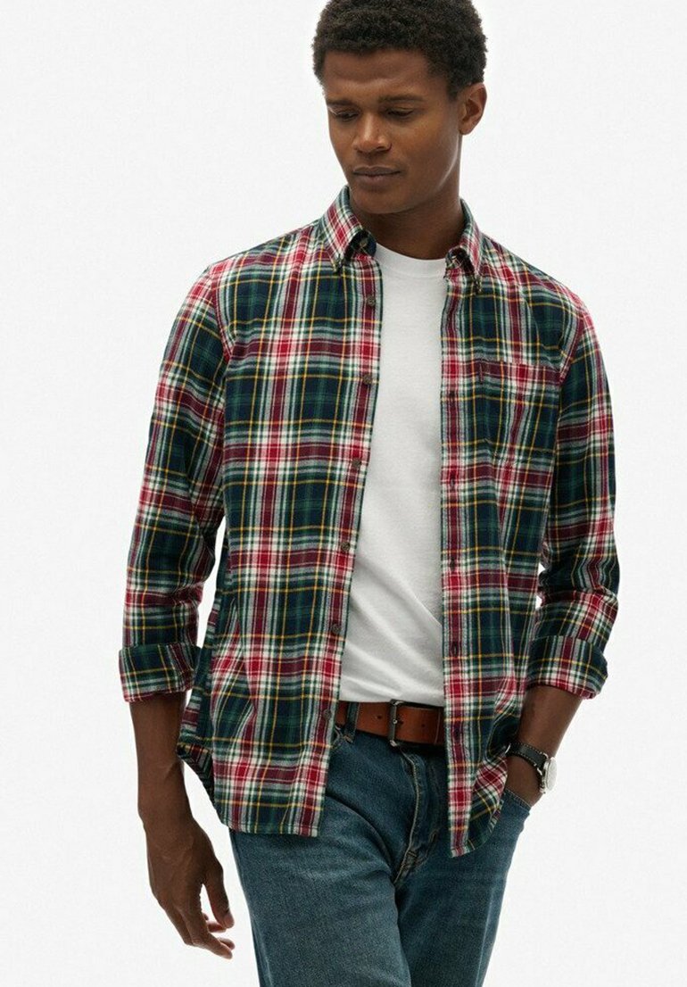 Camisa de cuadros con botones en un patrón de cuadros verde, rojo, amarillo y blanco, con mangas enrolladas y un bolsillo en el pecho, llevada sobre una camiseta blanca.