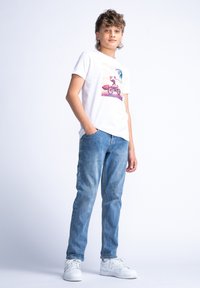 Camiseta blanca de manga corta con un estampado gráfico colorido que presenta a un ciclista, combinada con jeans azul claro y zapatillas blancas.