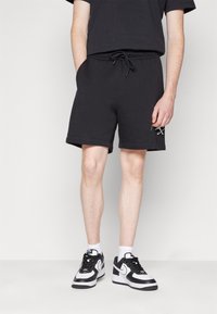 Černé bavlněné šortky na cvičení s elastickým pasem a šňůrkou, se bočními kapsami a minimalistickým logem na noze.