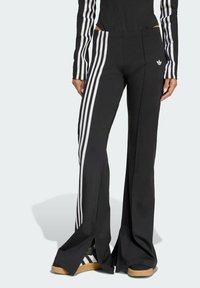 Black athletic pants featuring white triple stripes along the sides, flared leg design, and a small white logo on the hip.