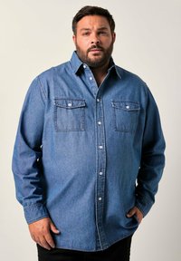 Camicia in denim blu con chiusura a bottoni, due tasche sul petto e maniche lunghe. Presenta un colletto classico e un taglio rilassato.