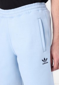 Svetlomodré bavlnené tepláky s elastickým pásom, dvoma bočnými vreckami a čiernym logom Adidas na ľavej nohe.