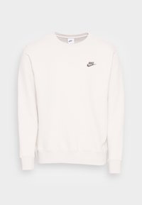 Sudadera de cuello redondo en color beige claro, con un sutil logo gris de Nike en el pecho, puños acanalados y una textura suave y lisa.