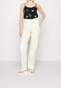 Haut caraco noir à imprimé floral, associé à un pantalon crème taille haute à jambes droites. Chaussures : sandales à plateforme blanches.