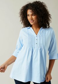 Ljusblå bomullspullover med V-hals, trekvarts ärmar, plankad frontdetalj och tre knappar vid halsen.