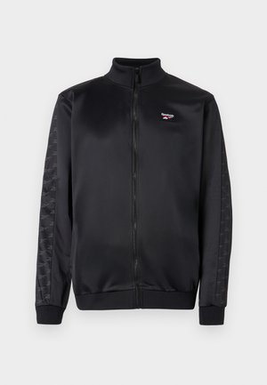 Sort Reebok zip-jakke med ribbet krave og manchetter, diskrete logo-striber langs ærmerne, og lille broderet Reebok-logo på brystet.
